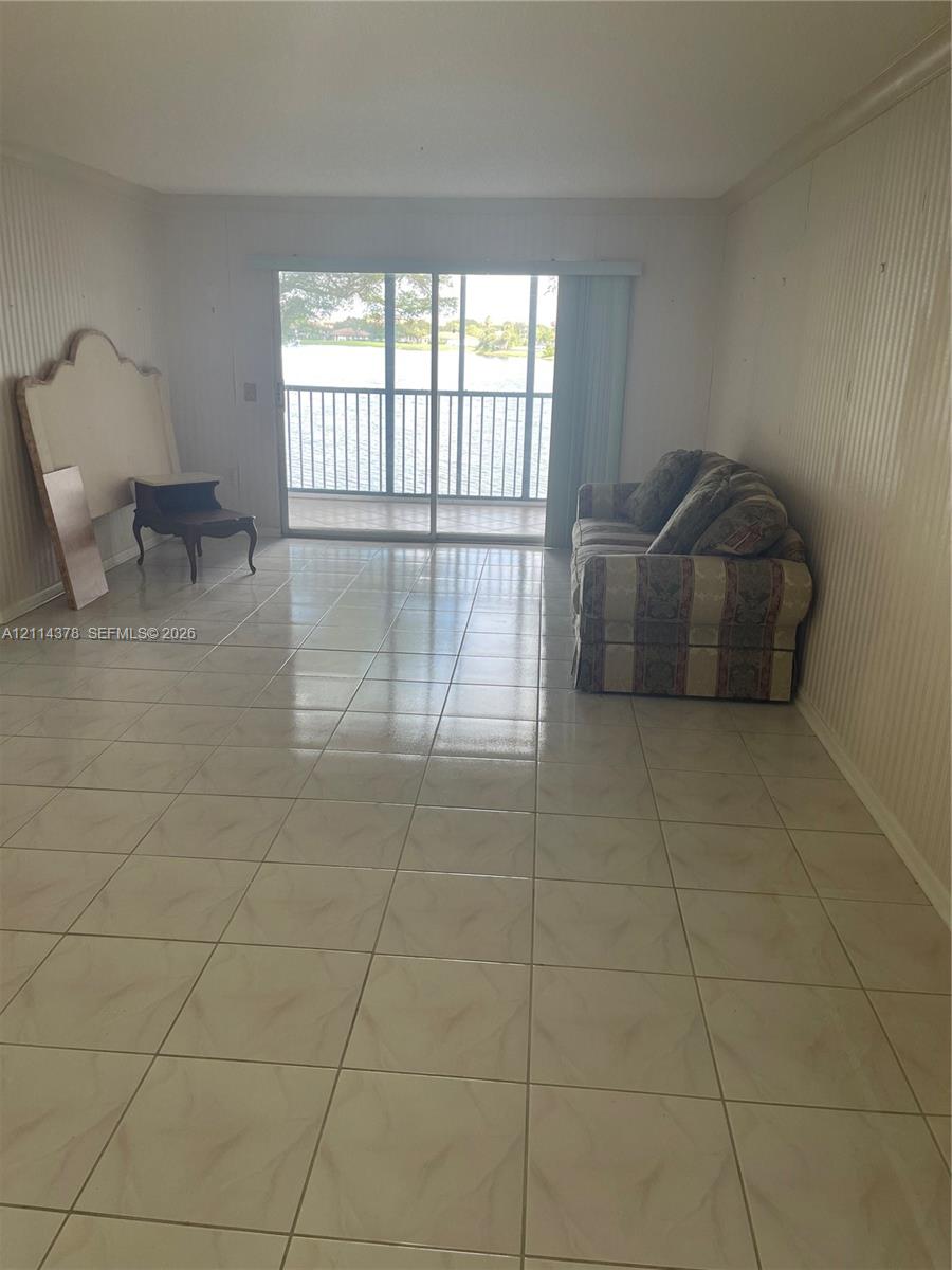 Interior space featuring light-toned ceramic tile flooring, vertical wall paneling, and large glass sliding doors leading to a screened balcony with water frontage