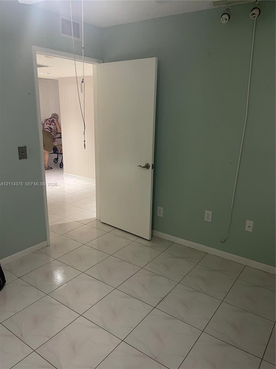 Room featuring large-format tile flooring, light green wall finishes, and a flush-mount interior door with metallic hardware