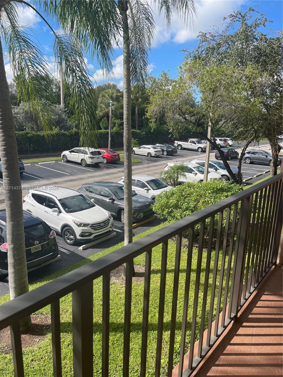 Balcony featuring a metal railing, overlooking a paved parking area with established palm trees and mature landscaping