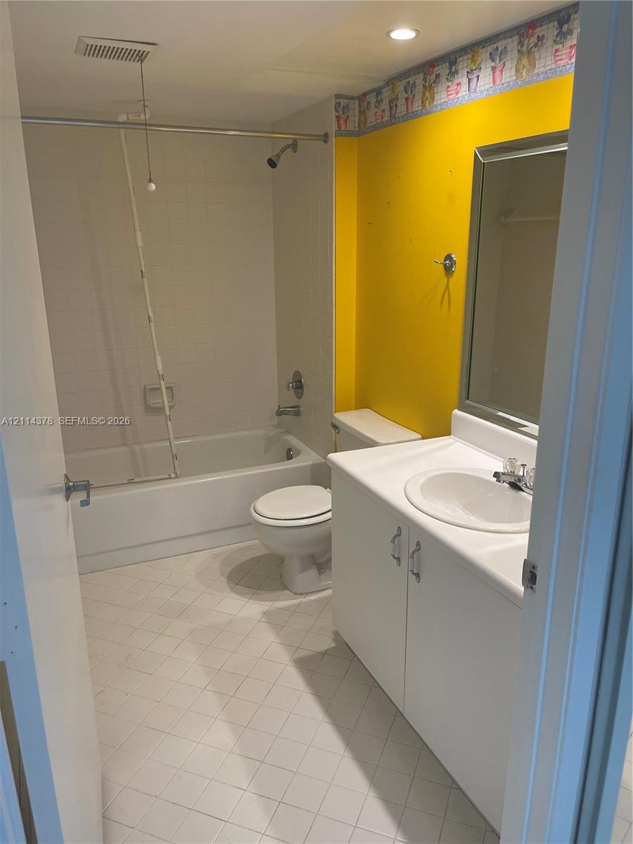 White vanity cabinet with integrated sink, porcelain tub and shower combination, and tiled flooring