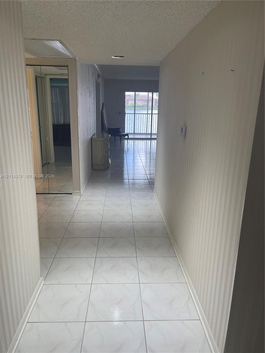 Interior corridor featuring large-format tile flooring, textured vertical wall surfacing, and mirrored sliding closet doors