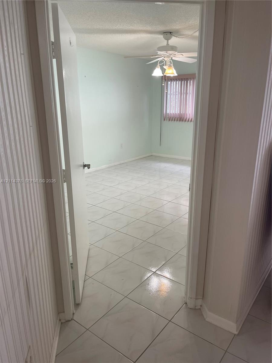 Interior space featuring polished ceramic tile flooring, a multi-blade ceiling fan with integrated light fixture, and vertical window blinds