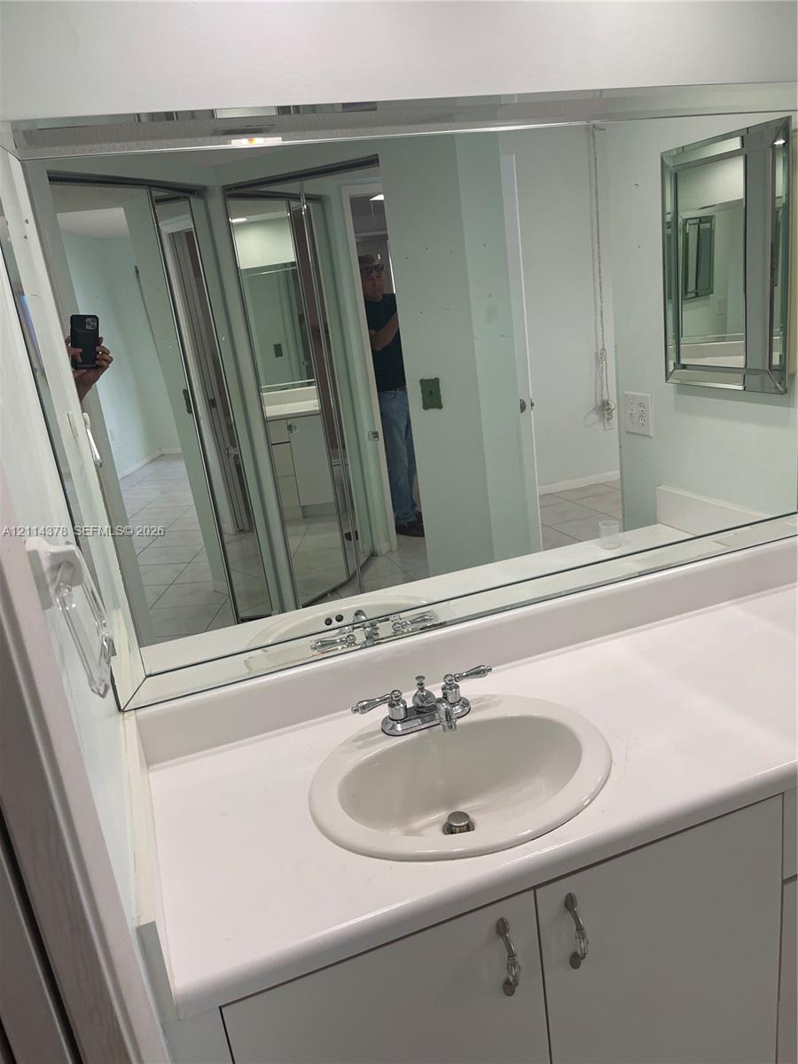 Vanity featuring a white countertop with an integrated oval sink, chrome dual-handle faucet, neutral cabinetry, and a full-width wall mirror with a beveled frame