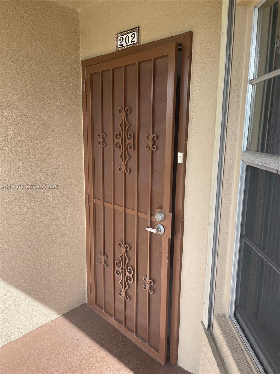 Brown metal security screen door featuring decorative scrollwork and a brushed-metal lever handle