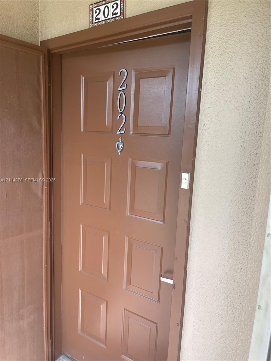 Solid-core door featuring eight recessed panels, metallic address numerals, a mounted door knocker, and an integrated doorbell