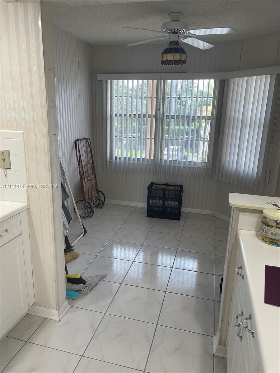Ceramic tile flooring, bay window with vertical blinds, and a ceiling-mounted light fixture with a fan