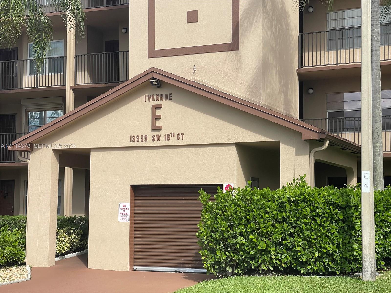 Multi-story residential building exterior featuring a stucco facade, covered entryway, private garage with a roll-up door, and iron balcony railings