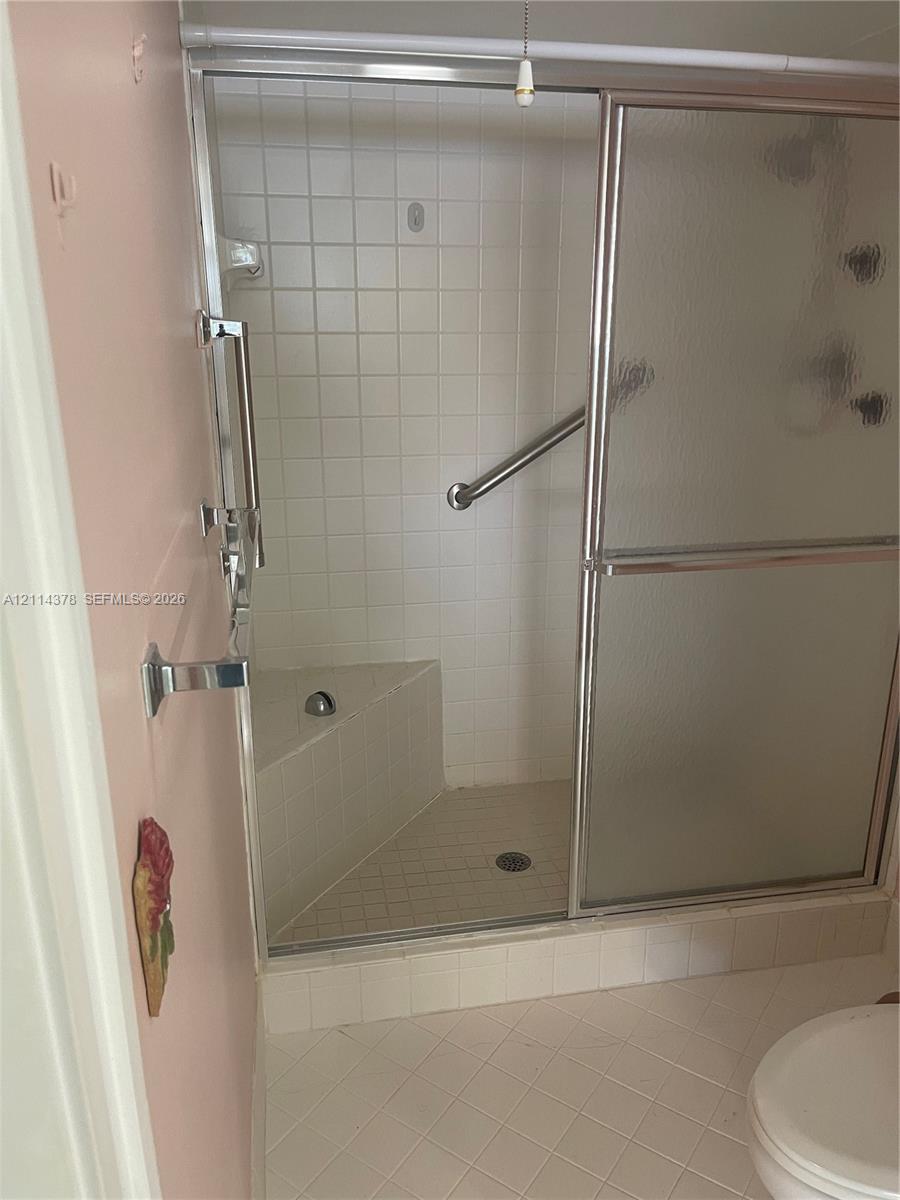 Walk-in shower featuring sliding glass doors, a built-in corner seat, tile surround, and chrome grab bars