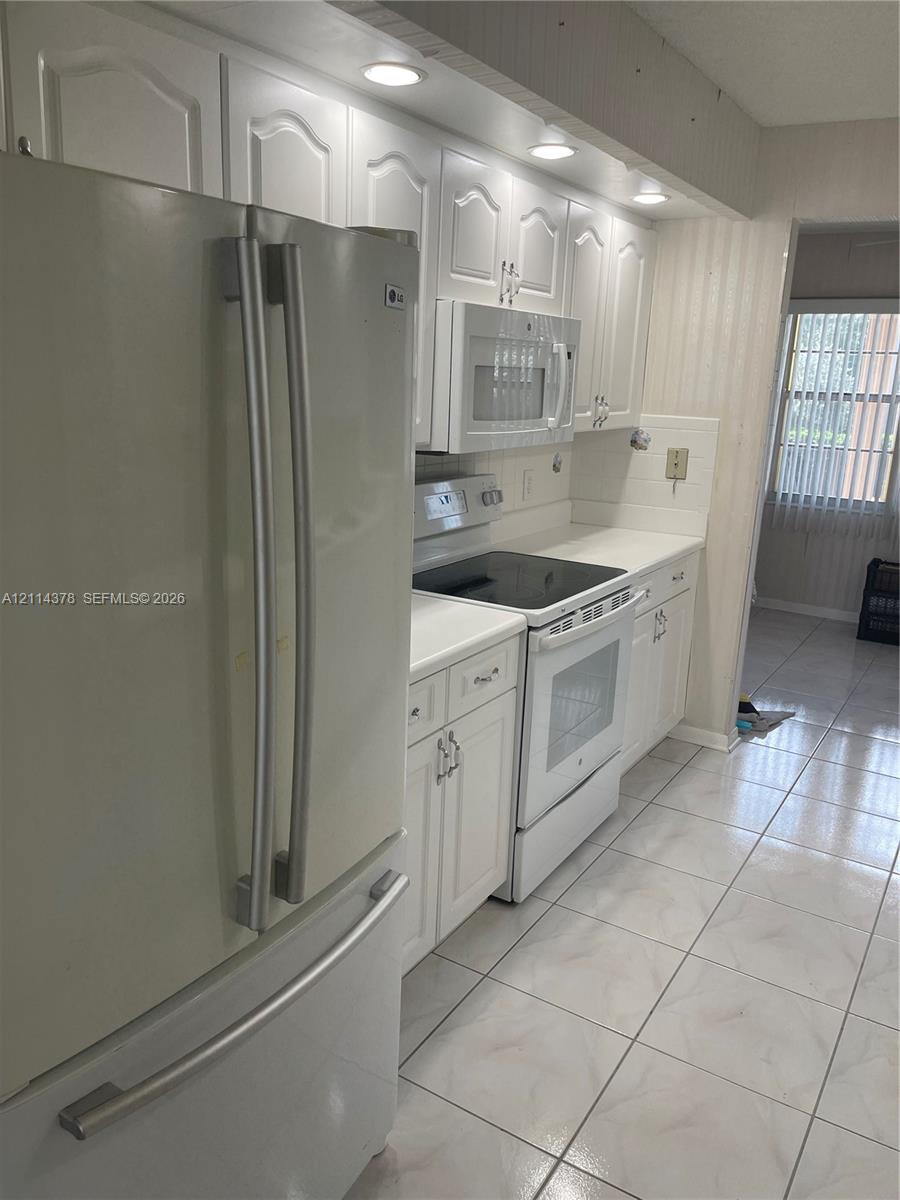 Kitchen featuring white cabinetry, tile flooring, recessed lighting, and white appliances including a built-in microwave and French-door refrigerator