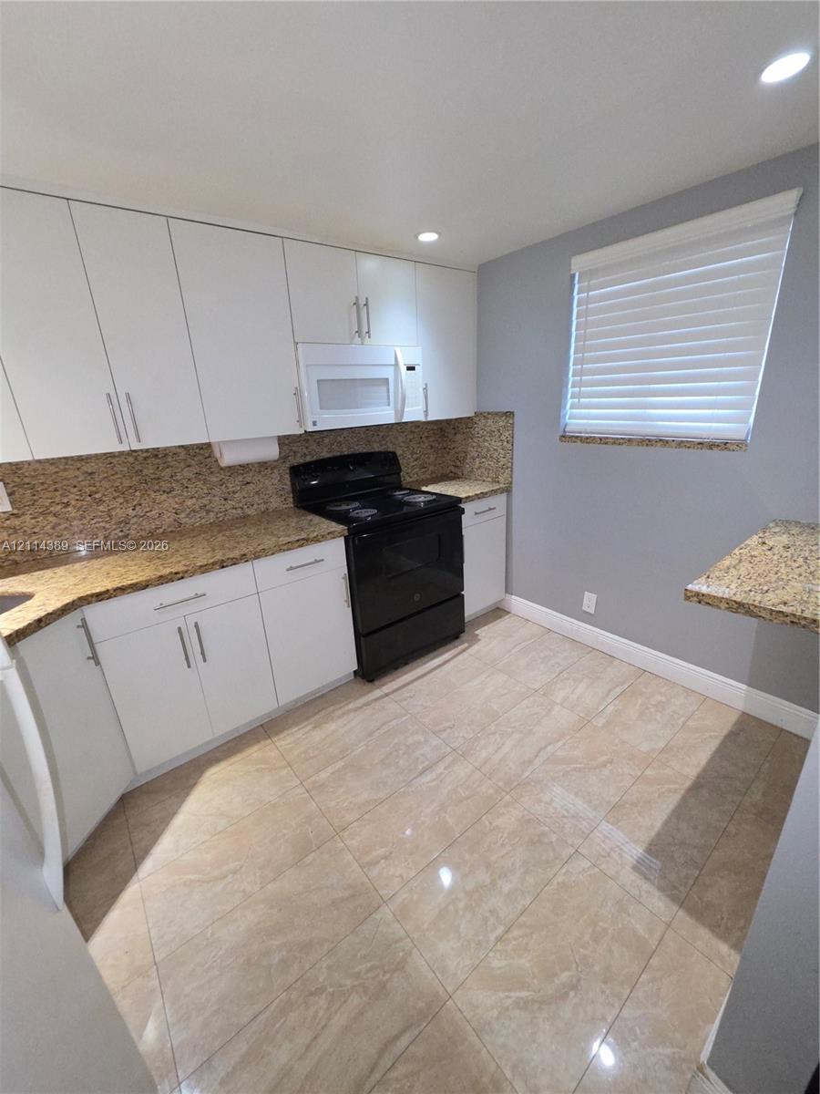 Kitchen featuring white cabinetry, stone-surface countertops, tile flooring, and integrated black range and microwave appliances