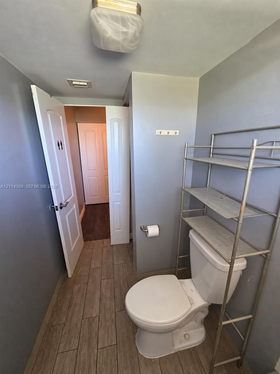 Wood-finish tile flooring, white porcelain toilet, and ceiling-mounted flush light fixture