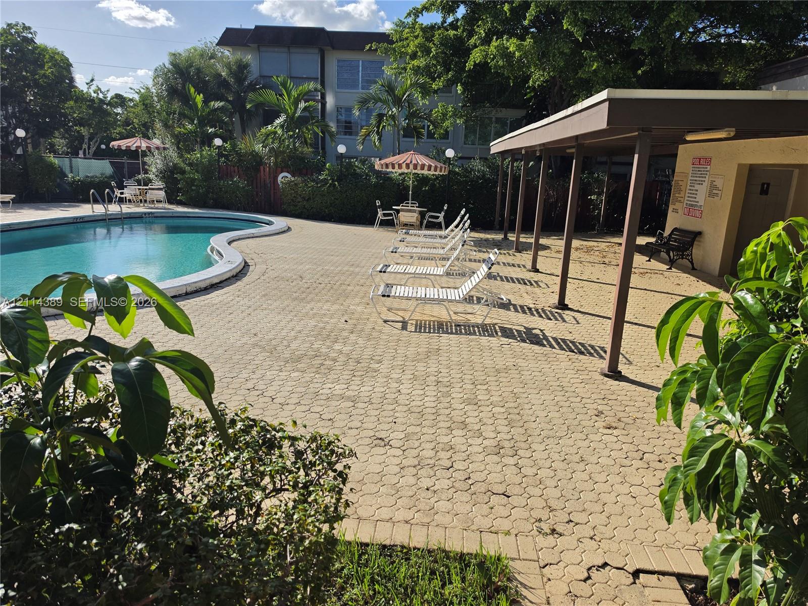Curved swimming pool with paver patio, covered pavilion, and mature landscaping