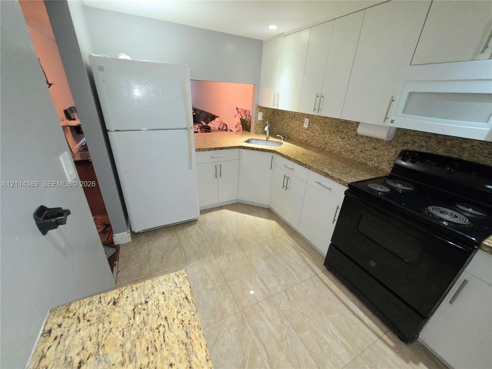 Kitchen featuring white cabinetry, stone-finish countertops, stone-tile flooring, and built-in appliances