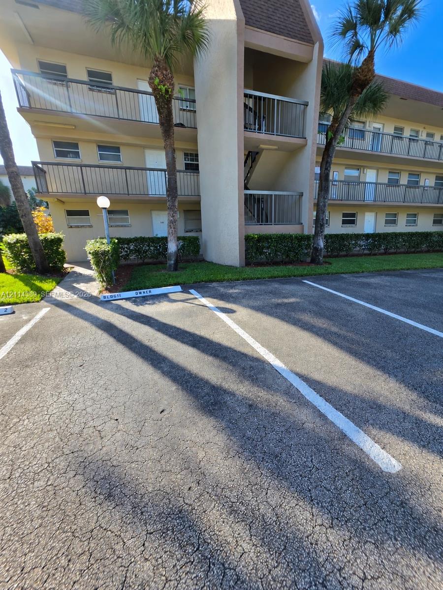 Multi-story exterior featuring metal railed balconies, paved parking area, and mature palm trees