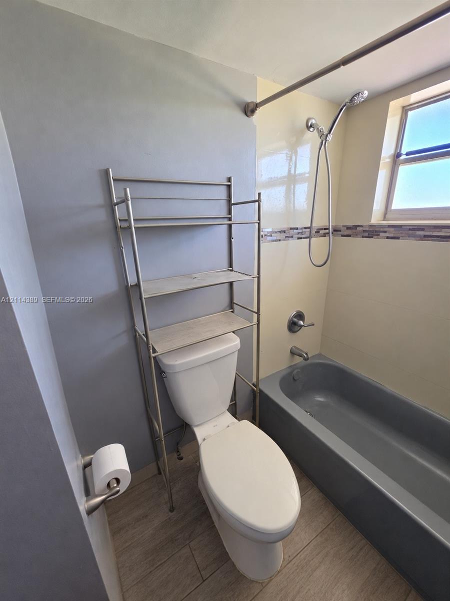Bathroom featuring wood-finish flooring, a porcelain bathtub with integrated tile surround, a single-handle chrome shower faucet, and a wall-mounted paper holder