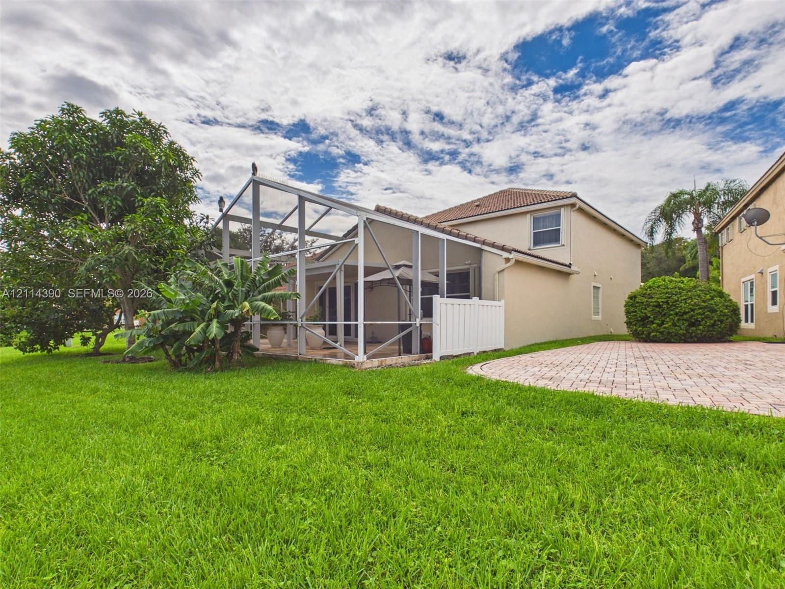 Screened-in lanai featuring a concrete patio, exterior stucco finish, tiled roof, and paver hardscaping