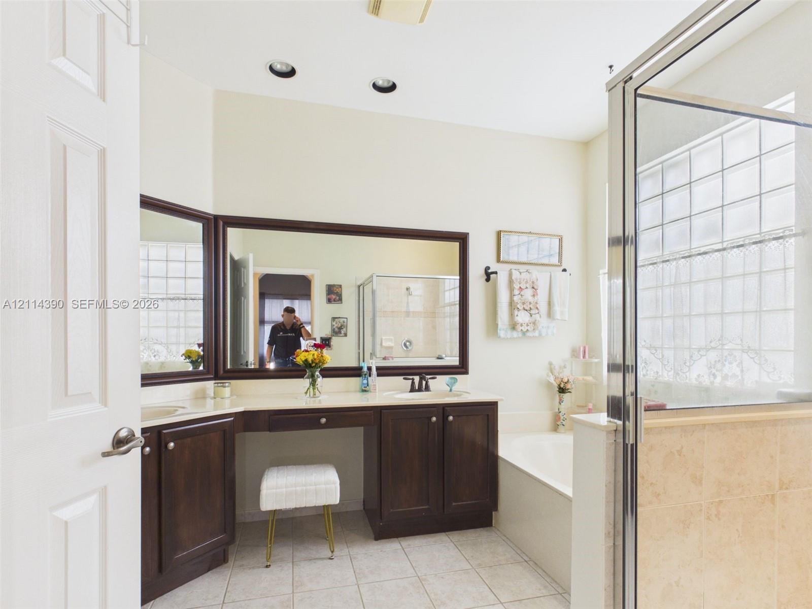Bathroom featuring a dual-sink vanity with dark wood cabinetry, large framed mirrors, a separate soaking tub, and a glass-enclosed shower with tiled surround