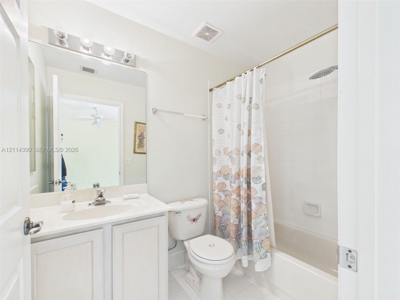 Bathroom featuring a white vanity cabinet with an integrated sink, full-width vanity mirror, polished chrome lighting fixture, and a tub-shower combination with white wall tile