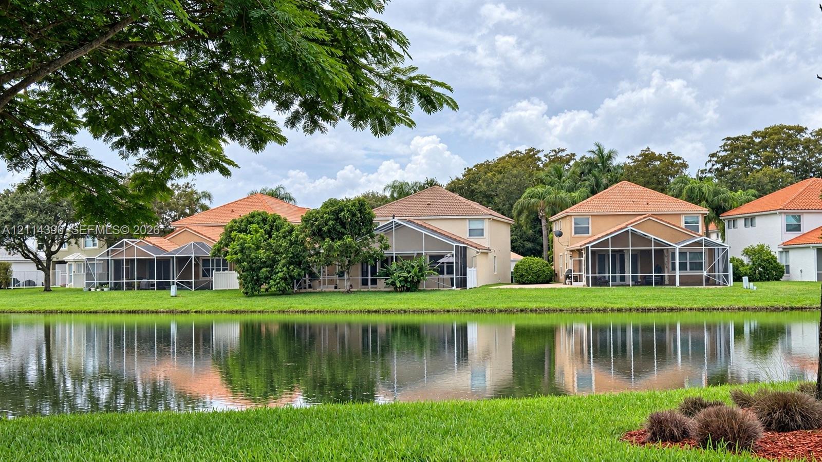 Waterfront property featuring screened-in lanais, tile roofs, and manicured landscaping