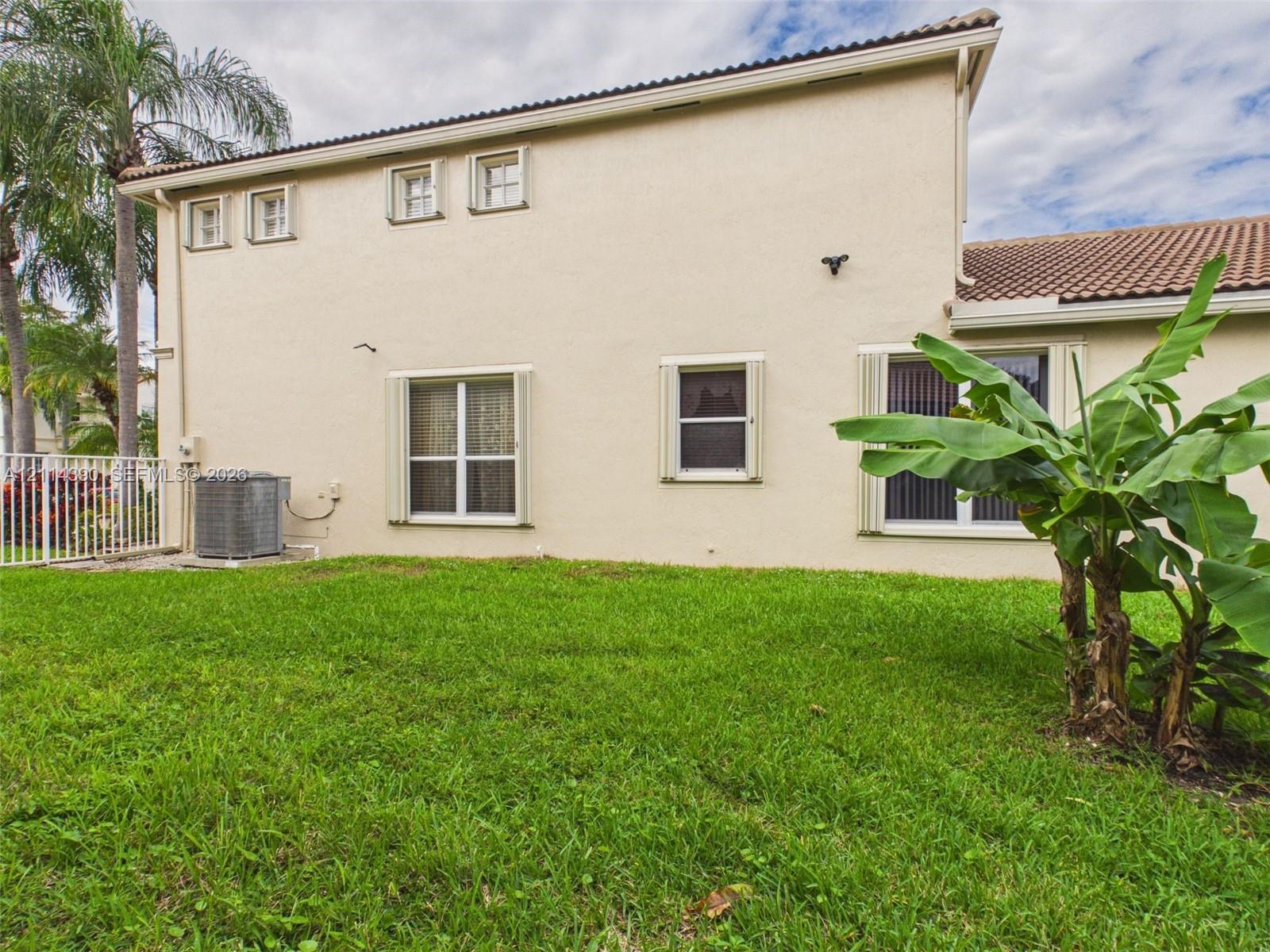 Stucco exterior featuring a tile roof, multiple multi-pane windows, and an outdoor HVAC unit, set against a manicured lawn