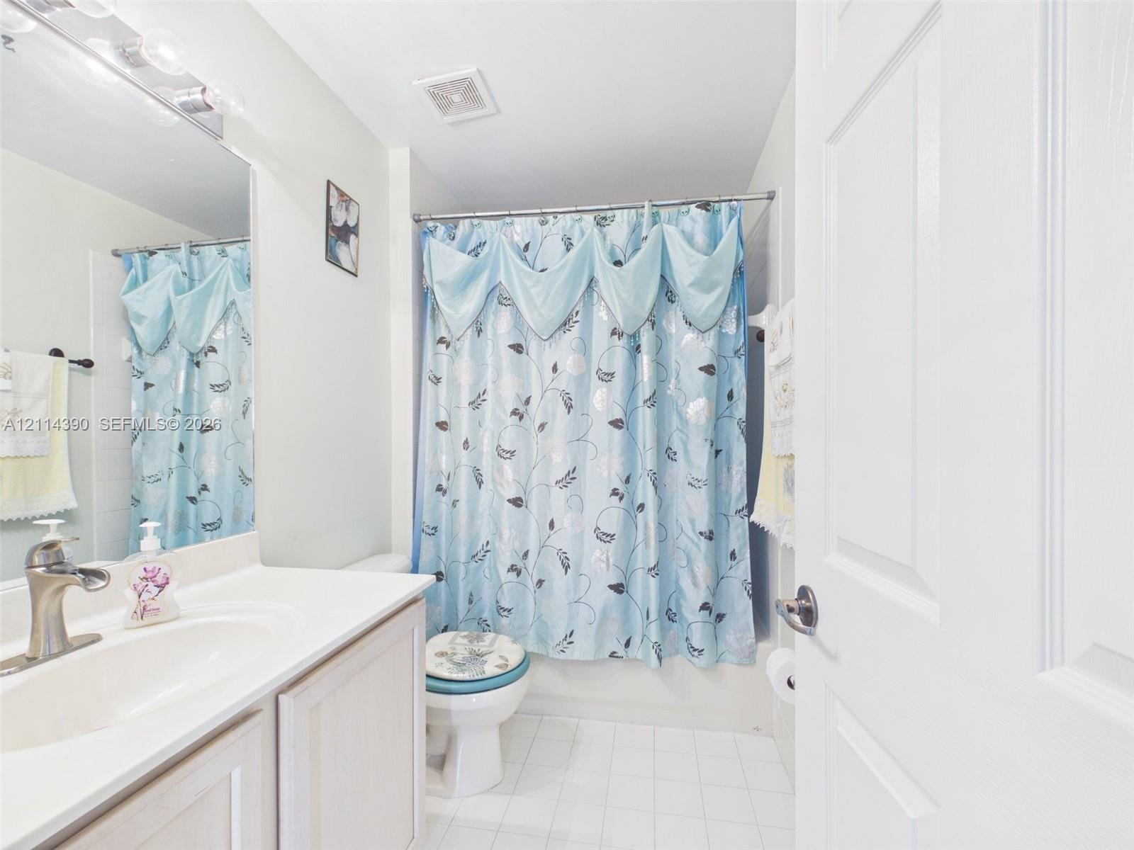 Bathroom featuring a vanity with an integrated sink, polished metal faucet, wide-frame wall mirror, and tile flooring