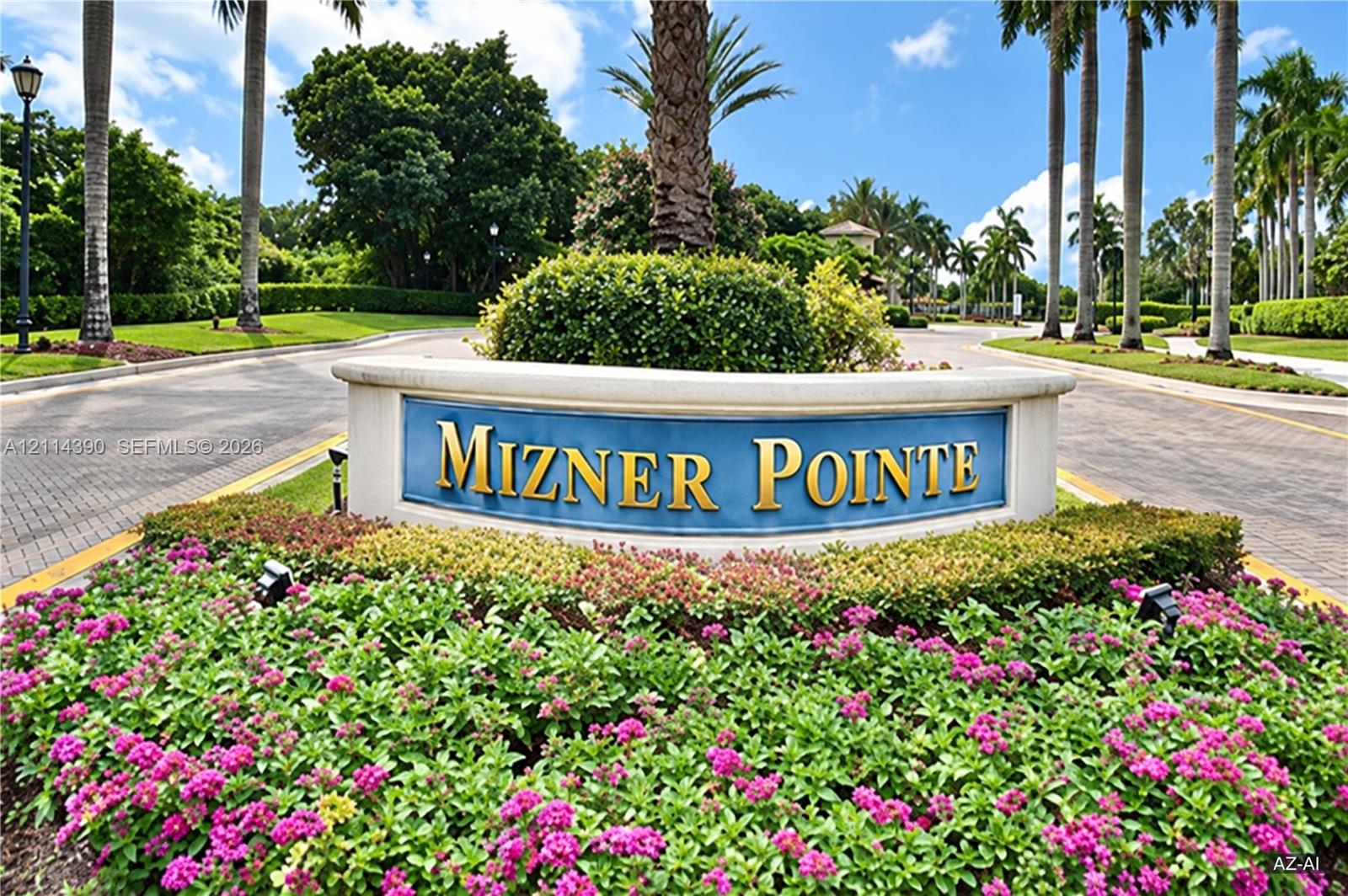 Mizner Pointe community entrance featuring a curved stone-finish monument sign, paved roadway, mature palm trees, and professional landscaping with flowering shrubbery