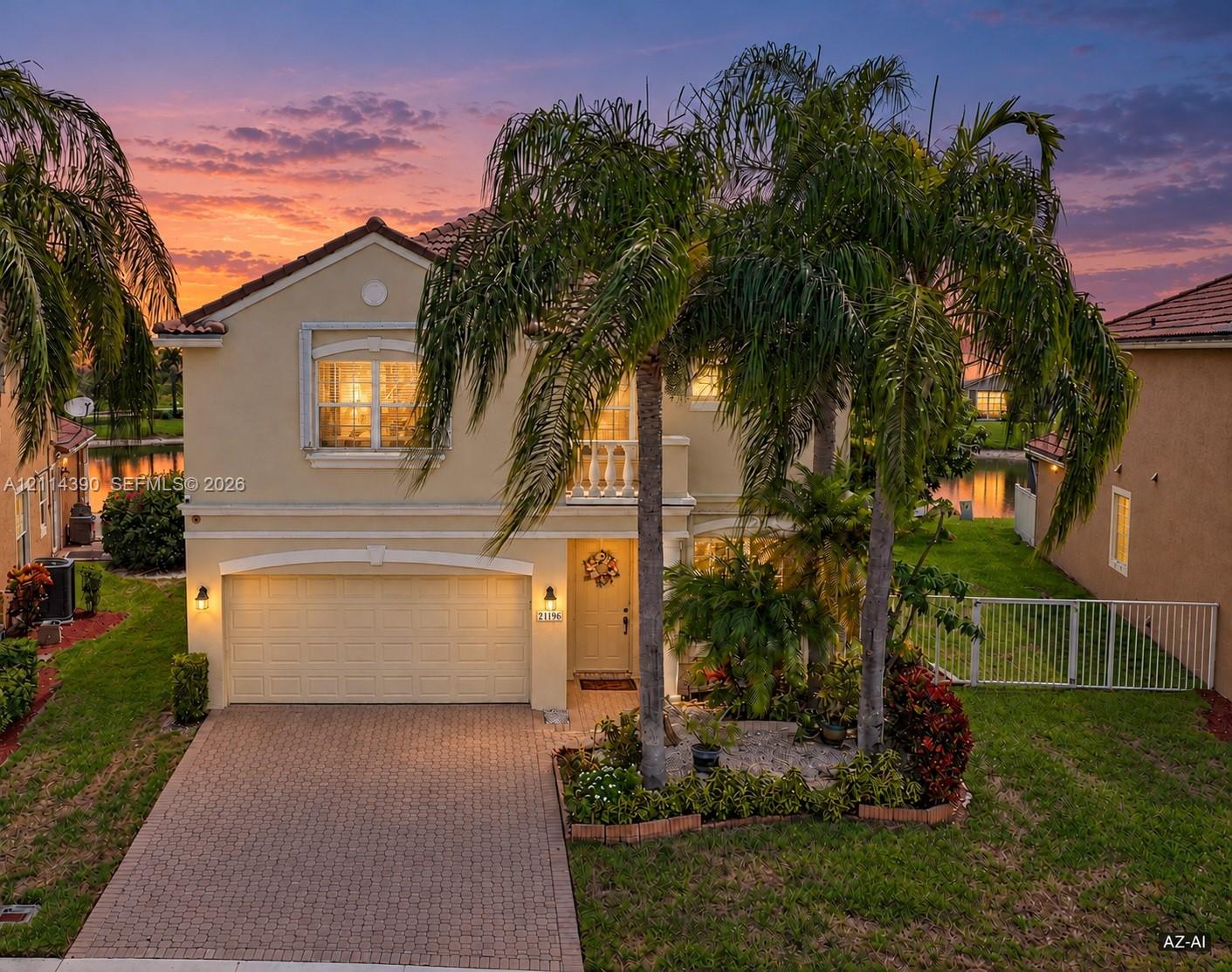 Two-story residence featuring a stucco exterior, paver driveway, second-story balcony with balustrade, attached two-car garage, and mature palm landscaping