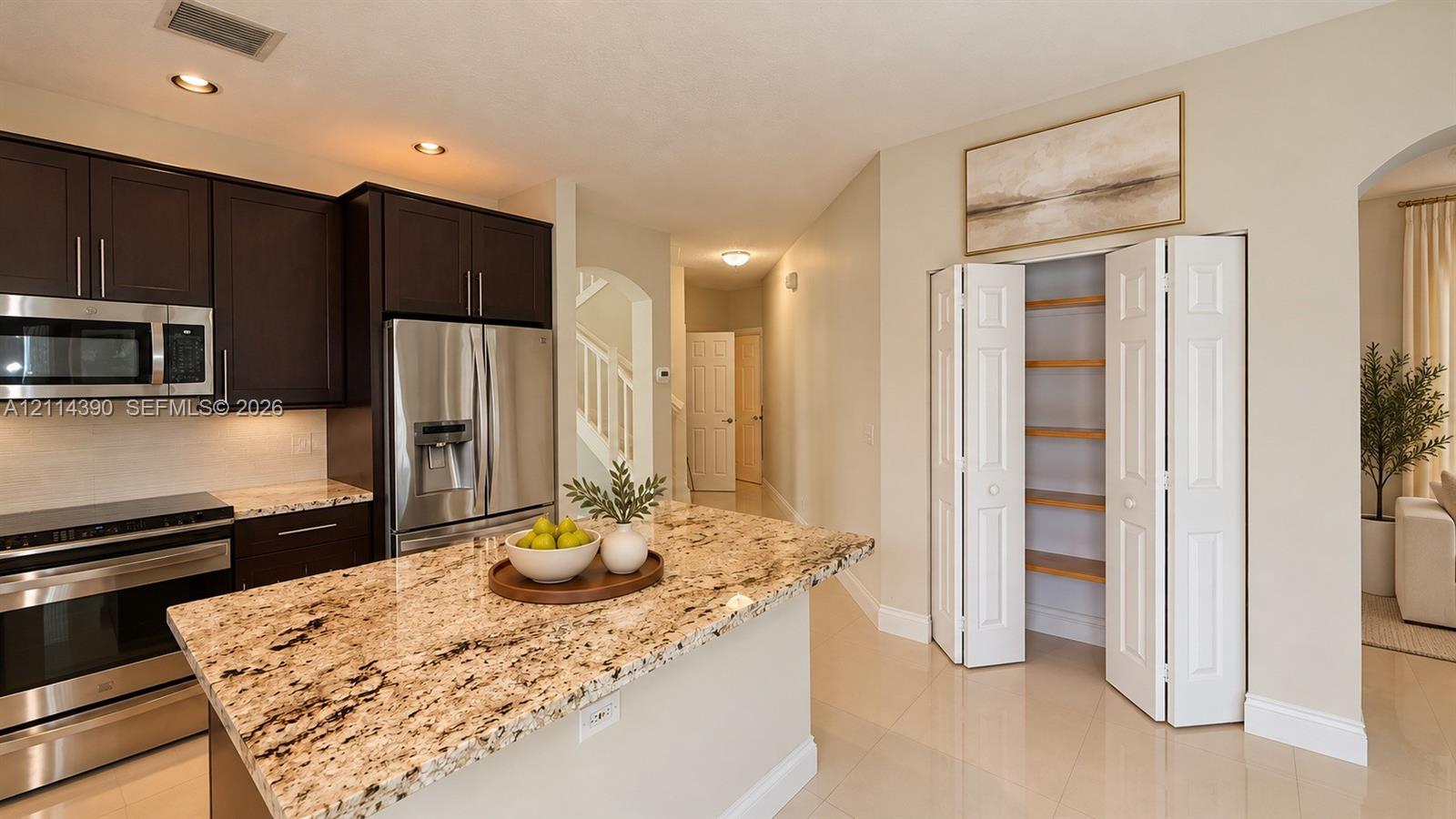 Kitchen featuring dark cabinetry, stone countertops, stainless steel appliances, a center island, and a built-in pantry with bi-fold doors
