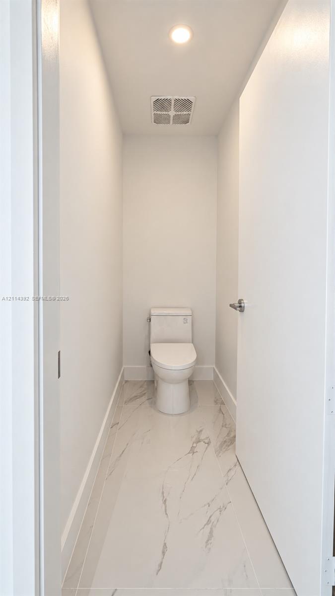 Minimalist water closet featuring large-format porcelain tile flooring with marble-style veining, a high-efficiency toilet, and recessed lighting