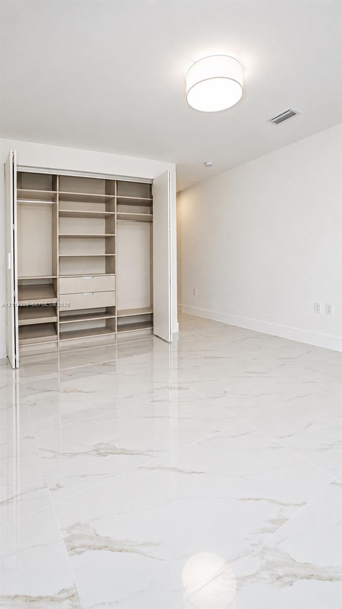 Large-format white tile flooring with veining, built-in closet organization system with integrated drawers and shelving, and flush-mount drum ceiling light