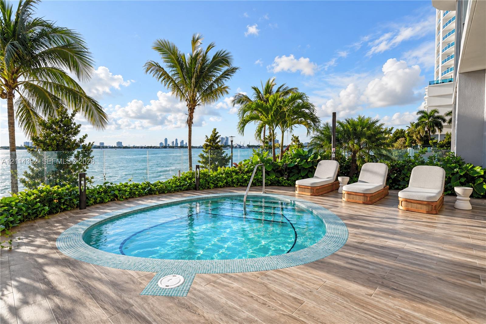 Oval-shaped swimming pool with tiled surround, wood-finish decking, glass panel railing, and mature palm landscaping