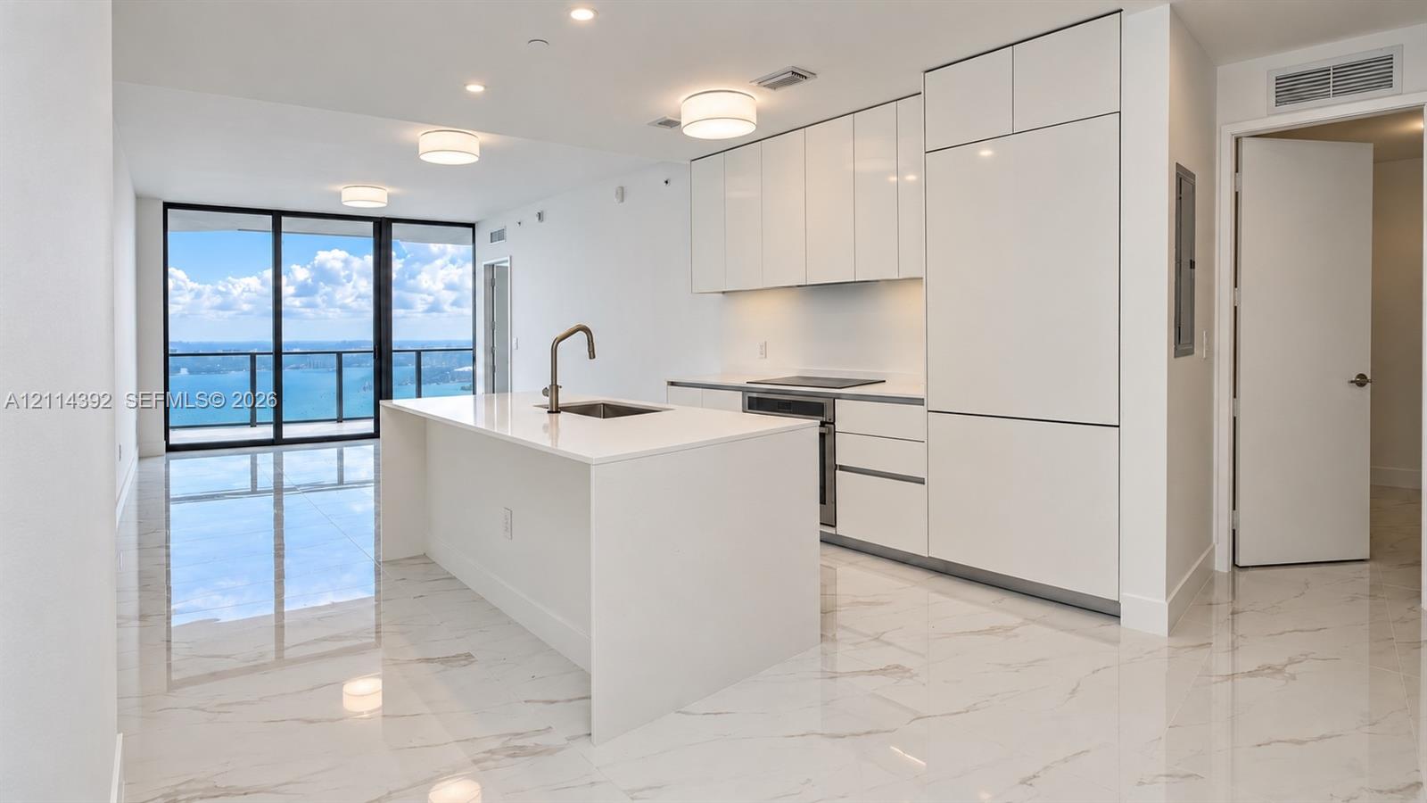 Modern kitchen featuring white flat-panel cabinetry, integrated appliances, a central island with a quartz countertop, and large-format porcelain tile flooring Modern kitchen featuring white flat-panel cabinetry, integrated appliances, a central island with a quartz countertop, and large-format porcelain tile flooring