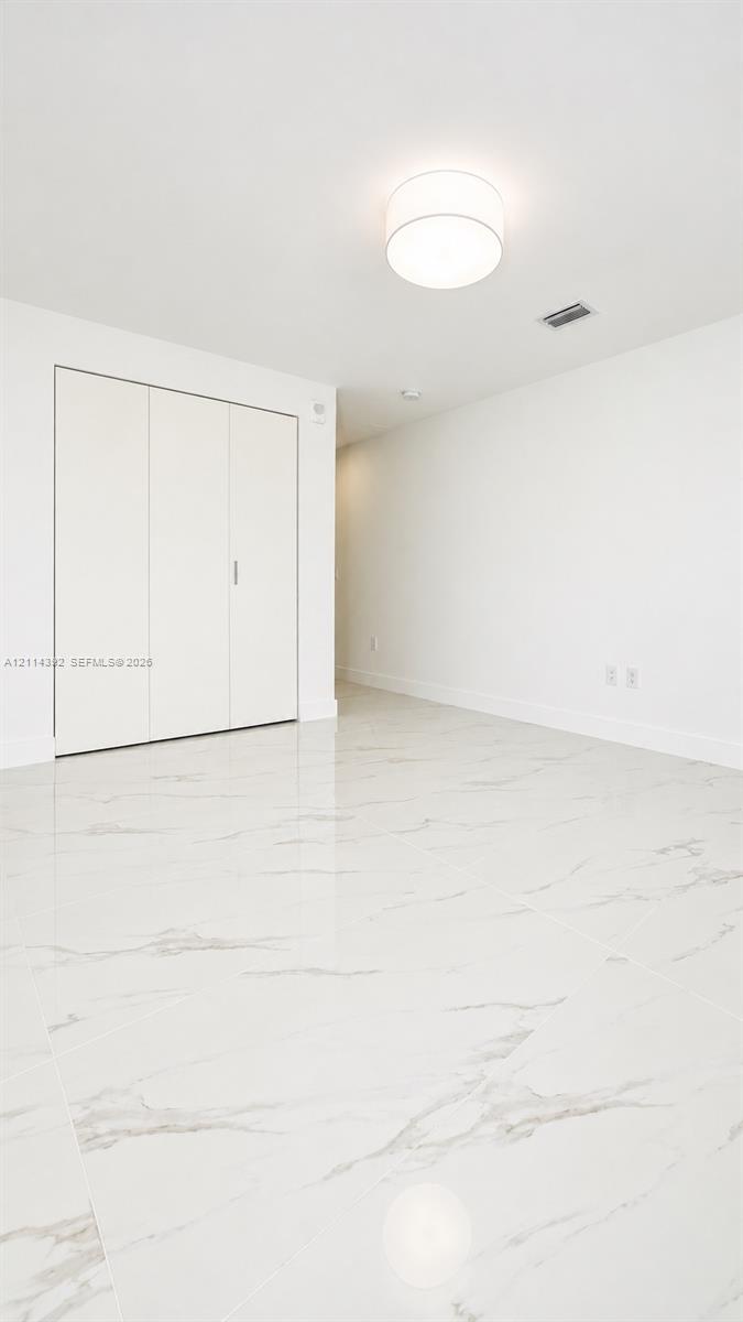 Polished stone-finish tile flooring, white walls, built-in closet with multi-panel doors, and a neutral drum-style ceiling fixture