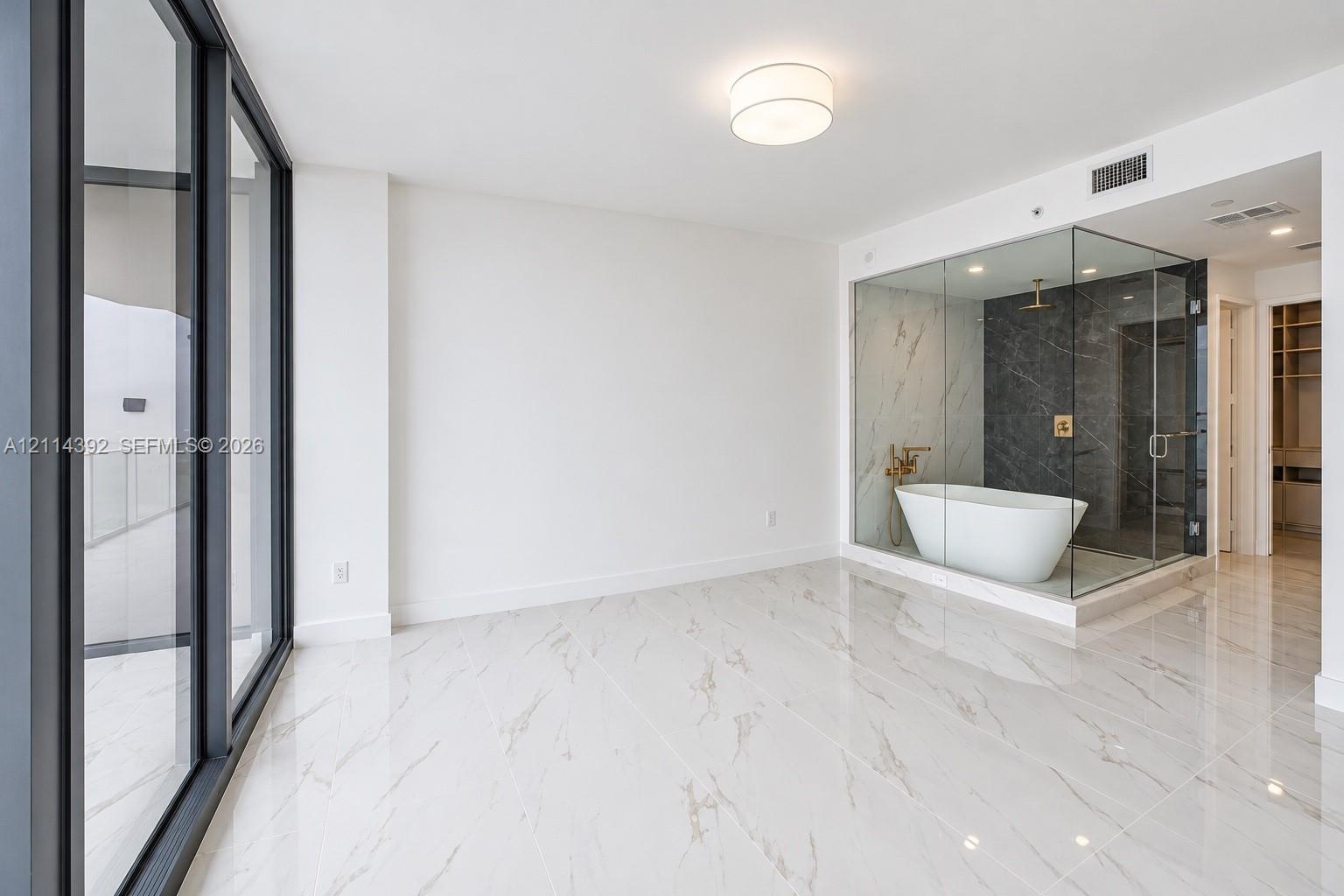 Floor-to-ceiling glass paneling, polished stone-finish flooring, glass-enclosed shower, freestanding soaking tub, and gold-tone fixtures Floor-to-ceiling glass paneling, polished stone-finish flooring, glass-enclosed shower, freestanding soaking tub, and gold-tone fixtures