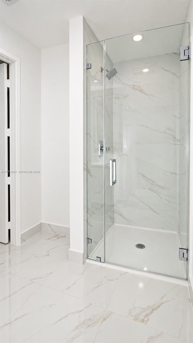 Walk-in shower featuring glass enclosure, wall-mounted rainfall showerhead, and large-format tile flooring and wall surfacing with veined detailing
