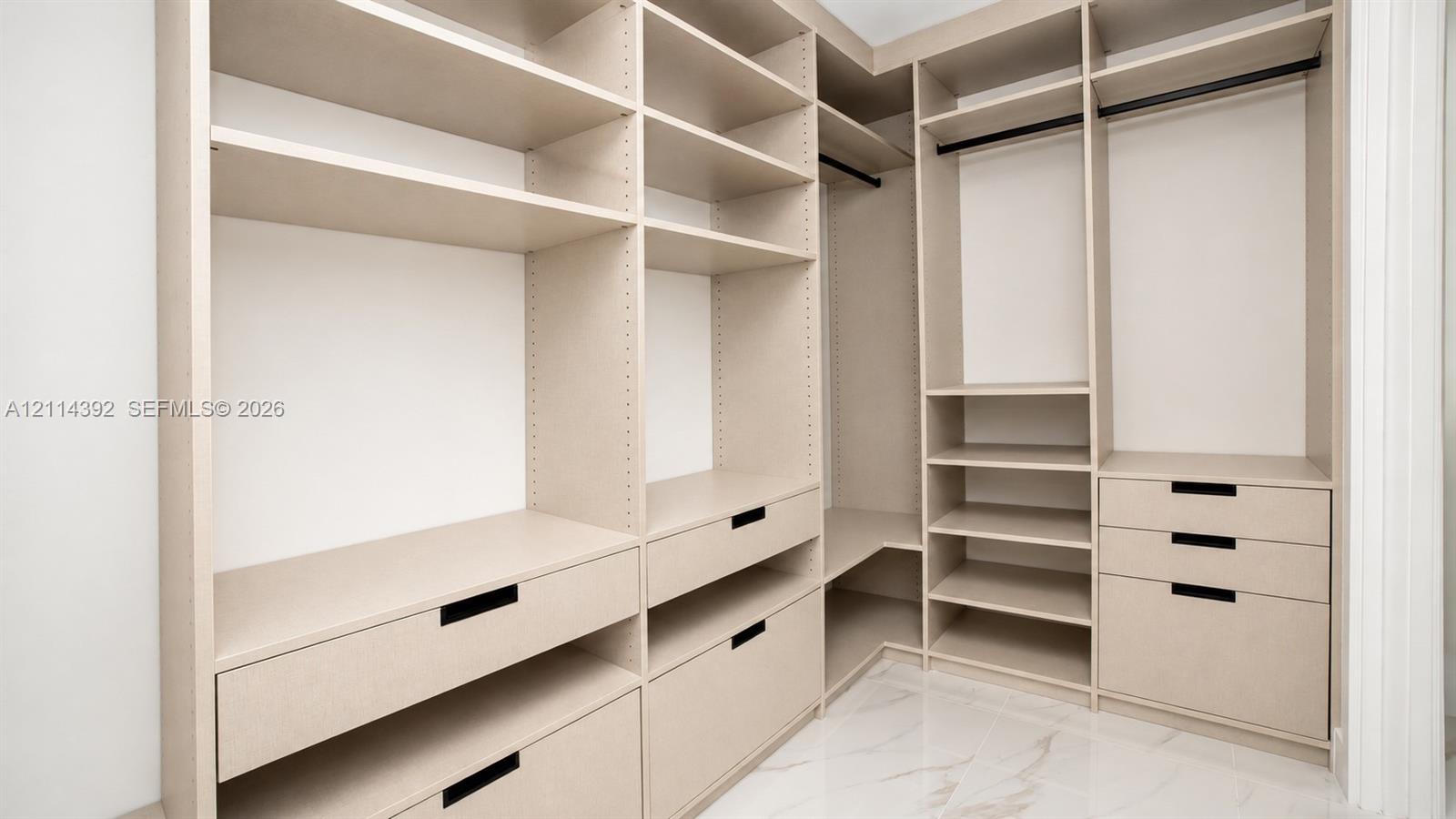 Custom walk-in closet featuring extensive built-in shelving, multiple integrated drawers with matte black pulls, dual hanging rods, and stone-finish flooring