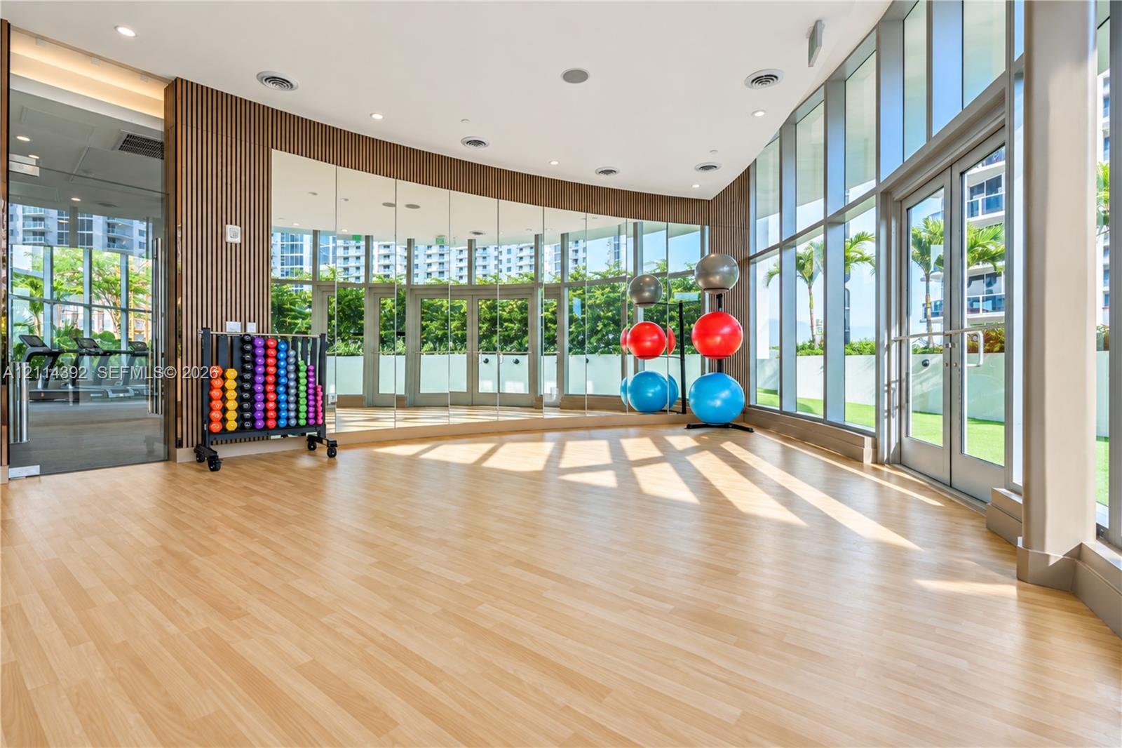 Fitness studio featuring floor-to-ceiling glass walls, wood-finish flooring, full-length mirror wall, and wood slat accent wall