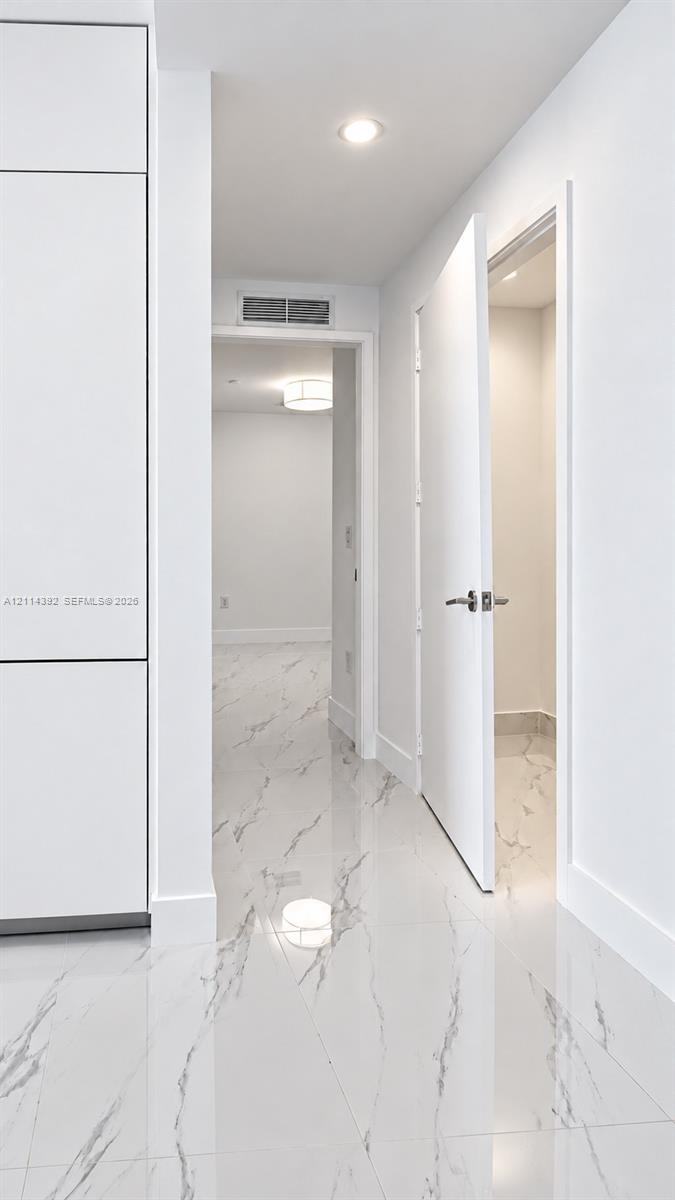 Polished stone-finish flooring with marbled detailing, full-height built-in cabinetry, recessed ceiling lighting, and solid-core interior doors with metallic hardware