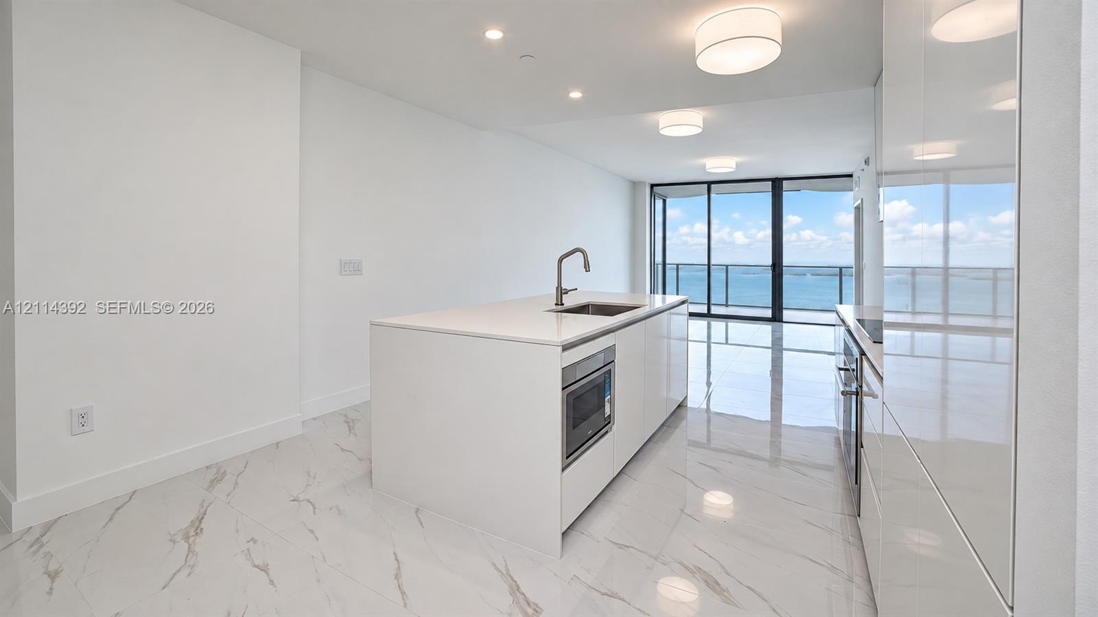 Kitchen featuring a central island with a quartz countertop, integrated microwave, undermount stainless steel sink, sleek high-gloss cabinetry, and light-toned tile flooring Kitchen featuring a central island with a quartz countertop, integrated microwave, undermount stainless steel sink, sleek high-gloss cabinetry, and light-toned tile flooring
