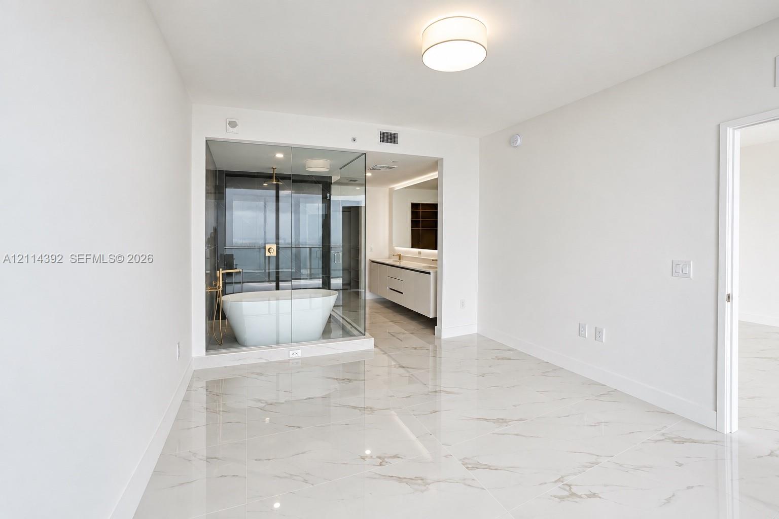 Polished stone-finish flooring, glass-enclosed bathroom area featuring a freestanding soaking tub, dual-sink floating vanity, and flush-mount lighting Polished stone-finish flooring, glass-enclosed bathroom area featuring a freestanding soaking tub, dual-sink floating vanity, and flush-mount lighting