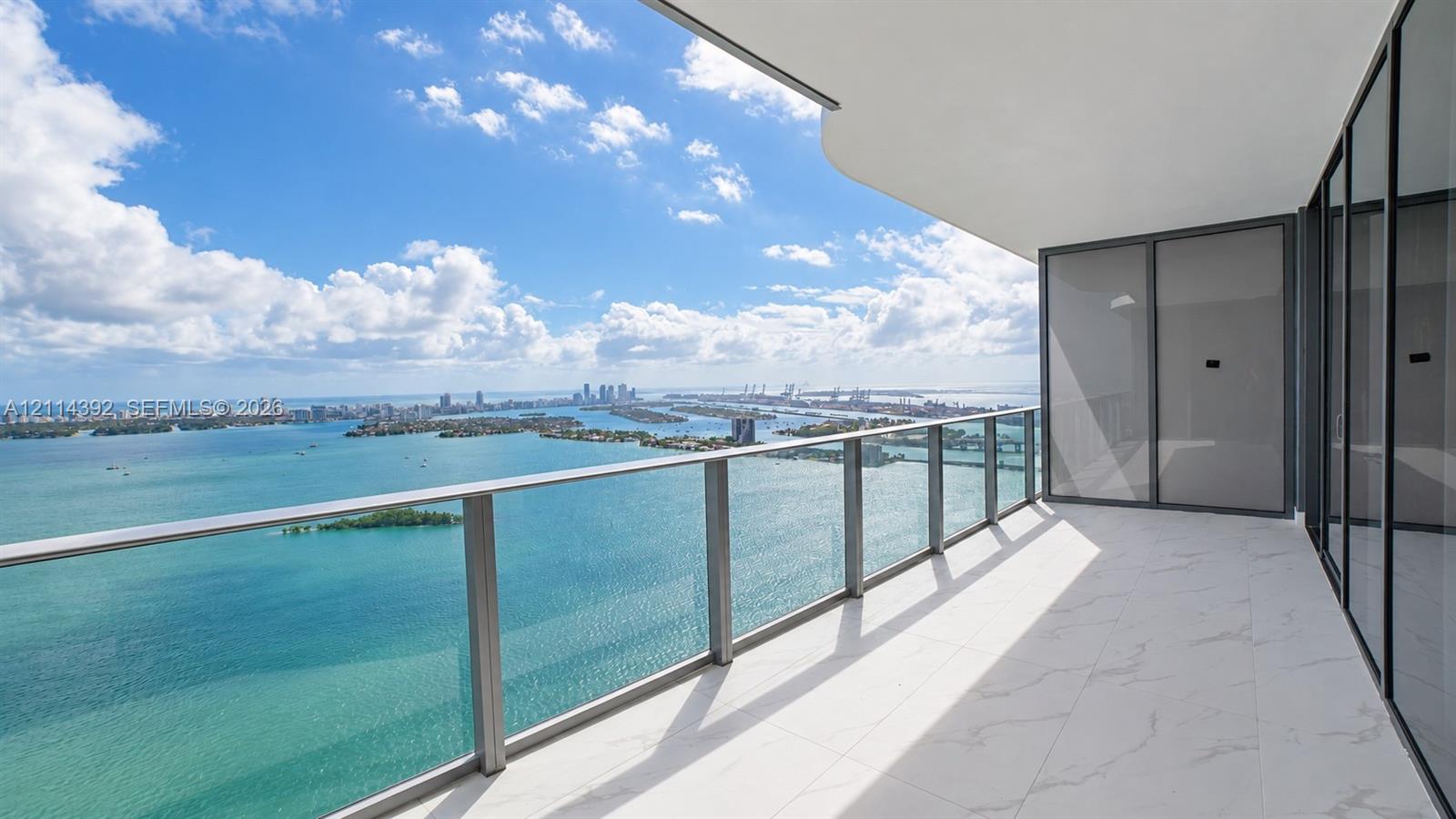 Covered balcony featuring white tiled flooring, metal-framed glass railings, and floor-to-ceiling glass wall panels Covered balcony featuring white tiled flooring, metal-framed glass railings, and floor-to-ceiling glass wall panels