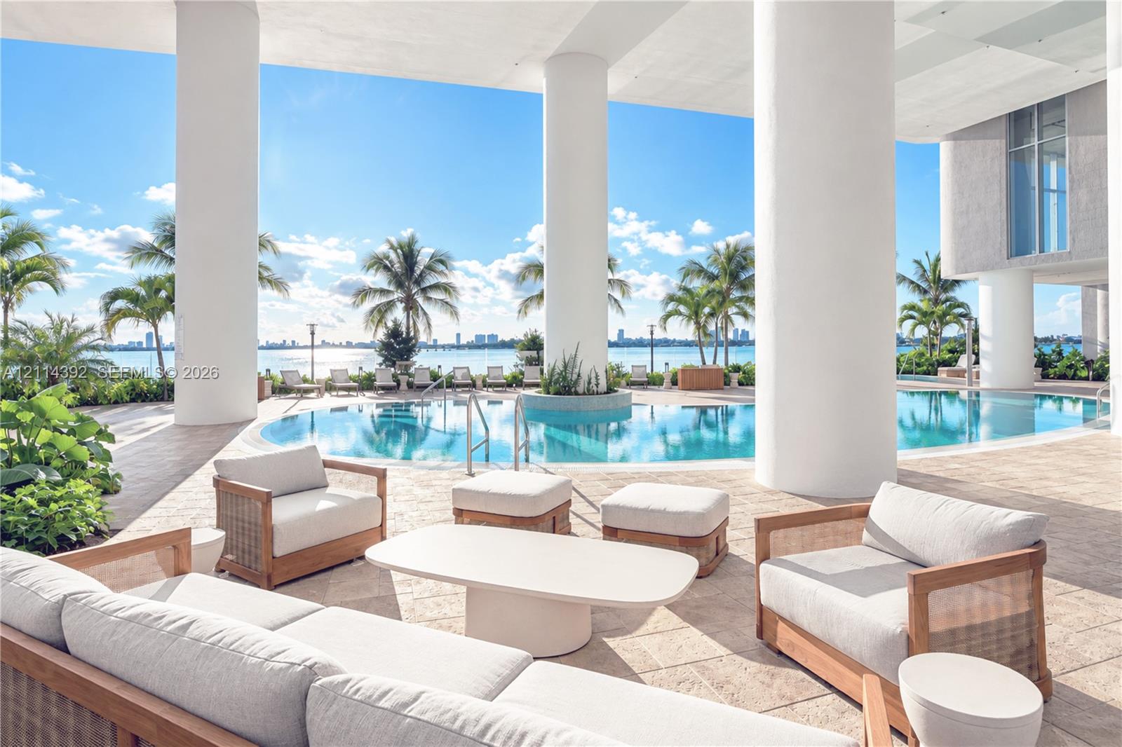 Covered terrace featuring natural stone flooring, oversized structural support columns, and access to an expansive outdoor pool with built-in planter