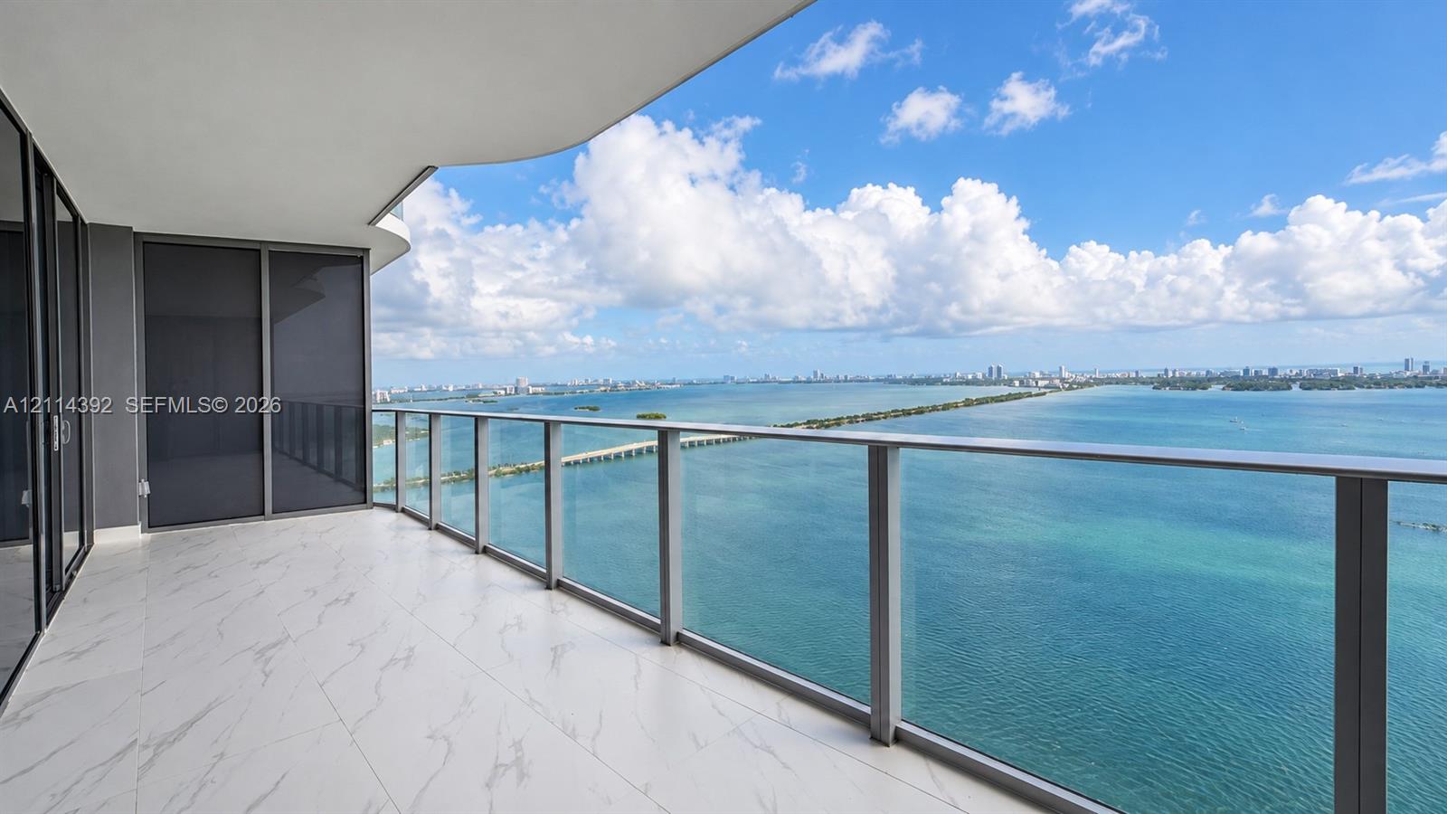 Expansive covered balcony featuring large-format stone-look tile flooring, a sleek glass railing system, and full-height glass panel doors Expansive covered balcony featuring large-format stone-look tile flooring, a sleek glass railing system, and full-height glass panel doors