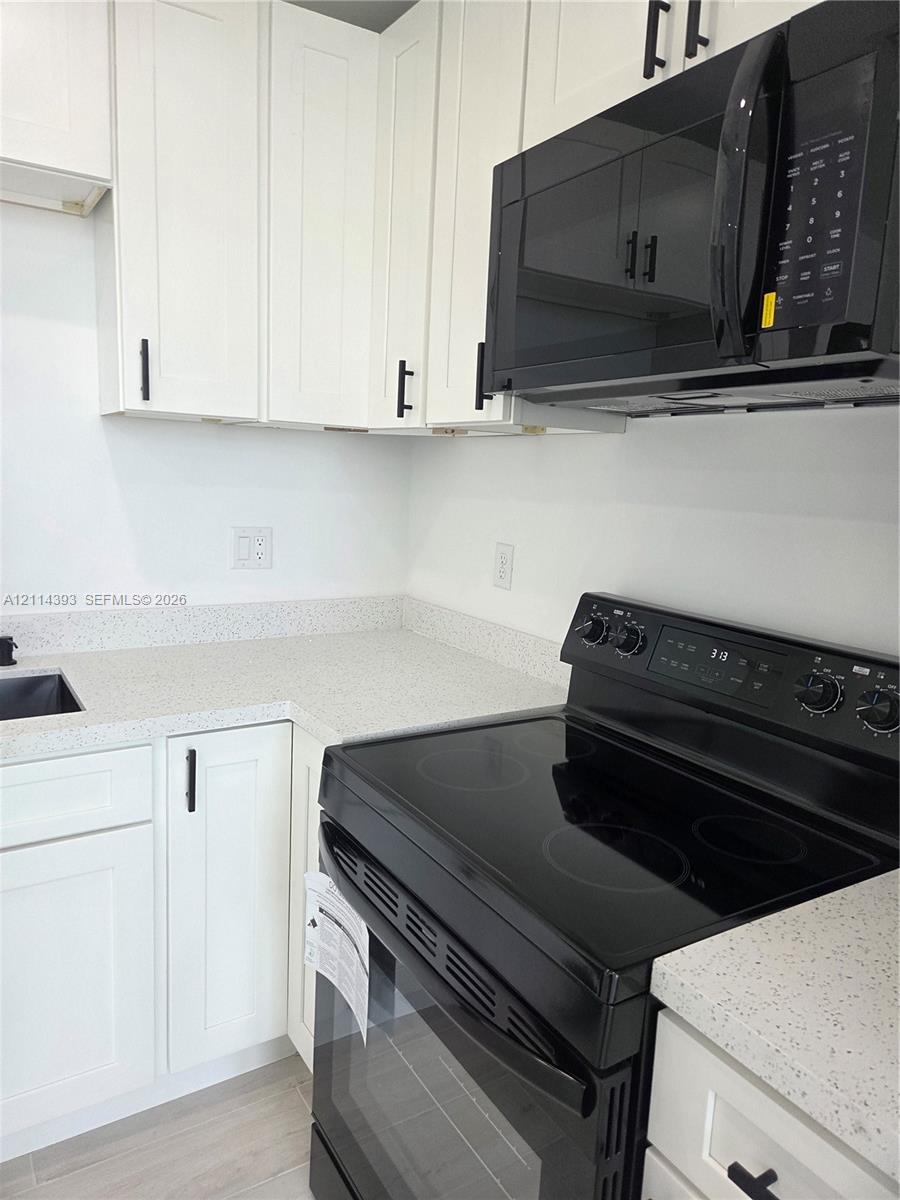 White Shaker-style cabinetry with matte black hardware, stone-composite countertops, built-in black over-the-range microwave, and matching black electric range
