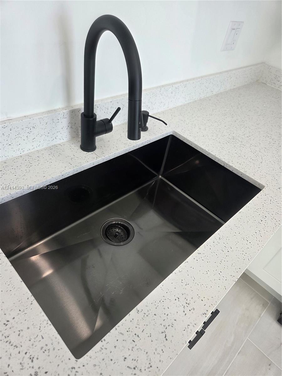 Undermount stainless steel sink featuring a matte black high-arc gooseneck faucet paired with a speckled stone-finish countertop
