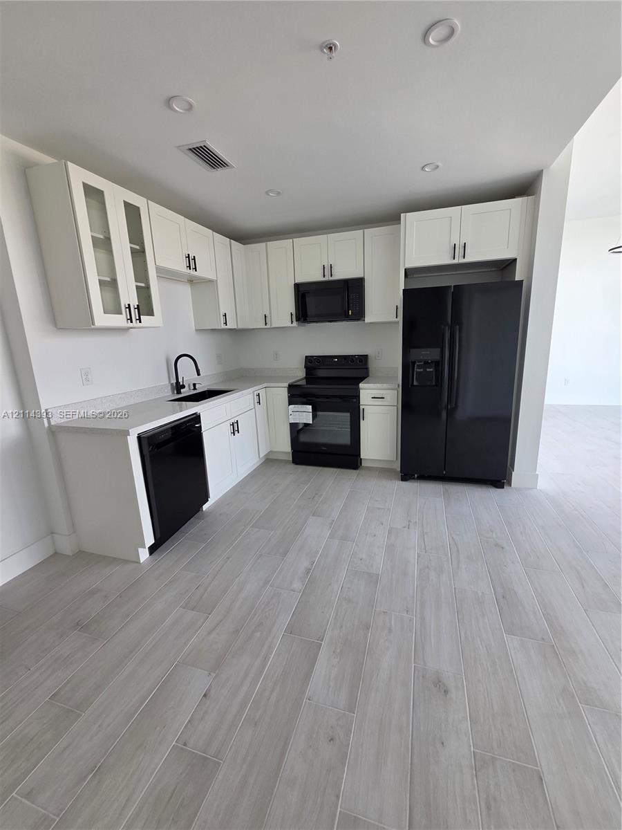 Kitchen featuring white shaker-style cabinetry, quartz countertops, black appliances, a gooseneck faucet, and wood-finish tile flooring