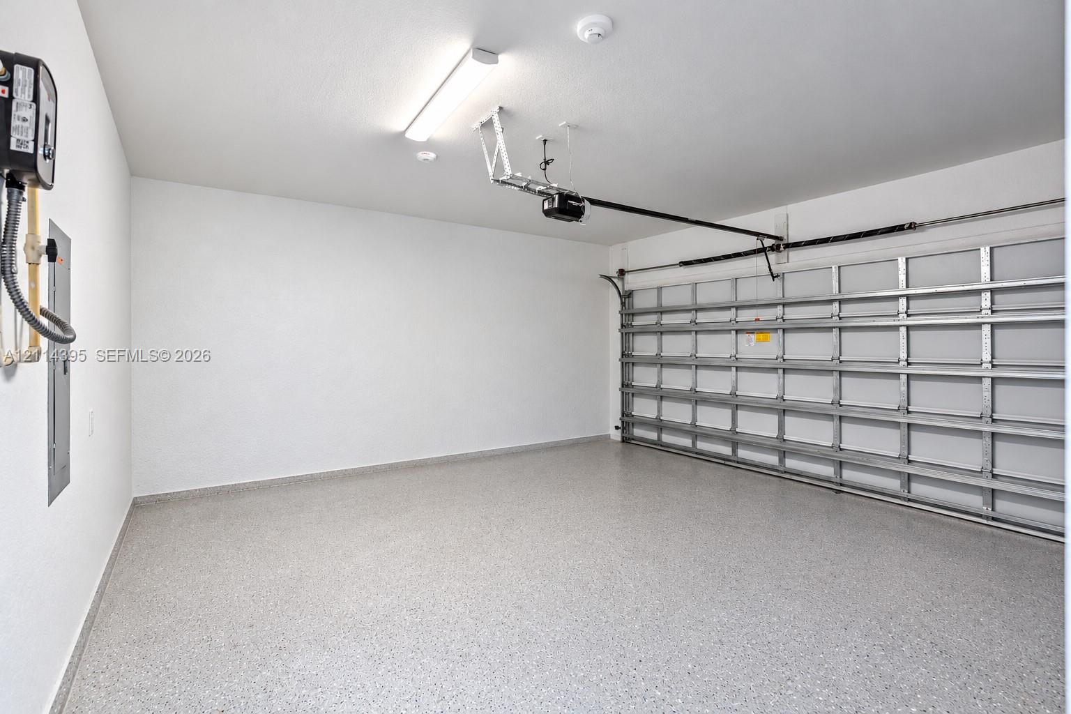 Garage space featuring epoxy-coated flooring, smooth white walls, an automated door opener, and overhead fluorescent lighting
