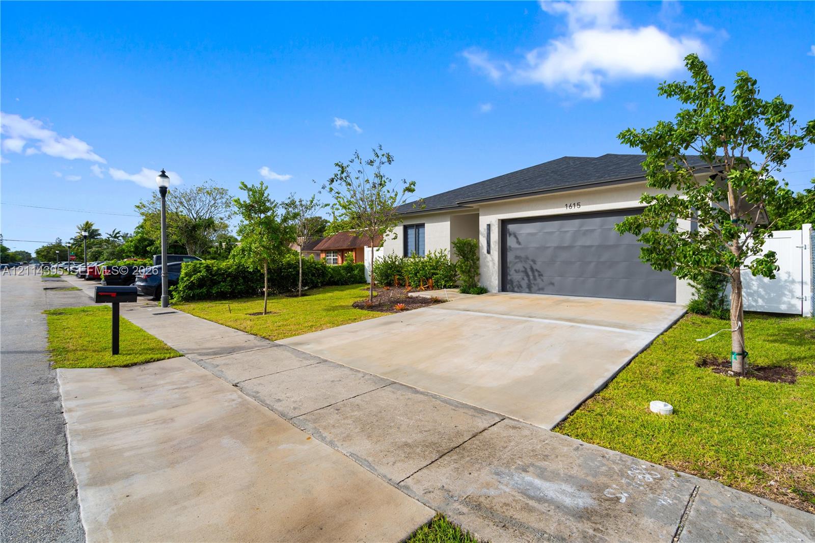 Single-story exterior featuring a concrete driveway, two-car garage, manicured lawn, and white privacy fencing Single-story exterior featuring a concrete driveway, two-car garage, manicured lawn, and white privacy fencing