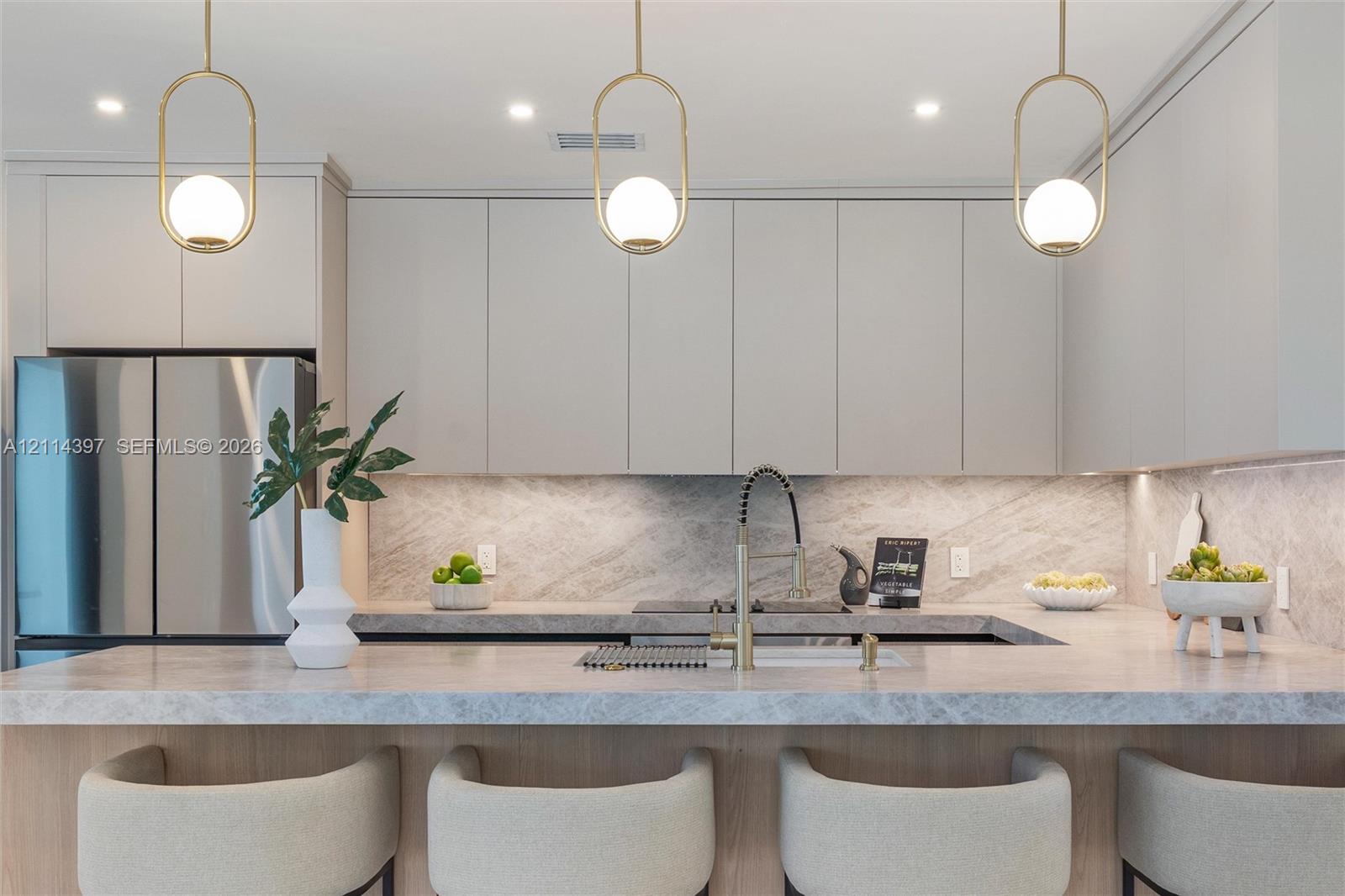 Kitchen featuring custom flat-panel cabinetry, stone countertops with matching full-height backsplash, gold-tone hardware, and three pendant lights with spherical glass globes