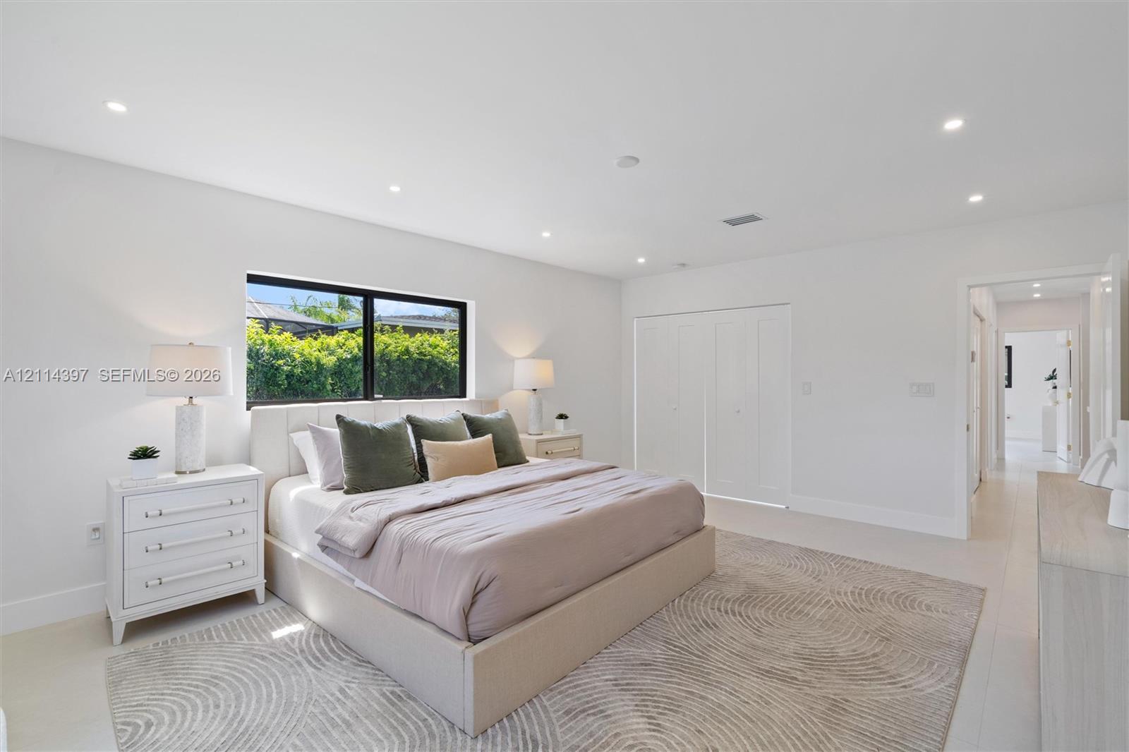 Neutral-toned room featuring recessed lighting, a large window with black framing, and multi-panel interior closet doors